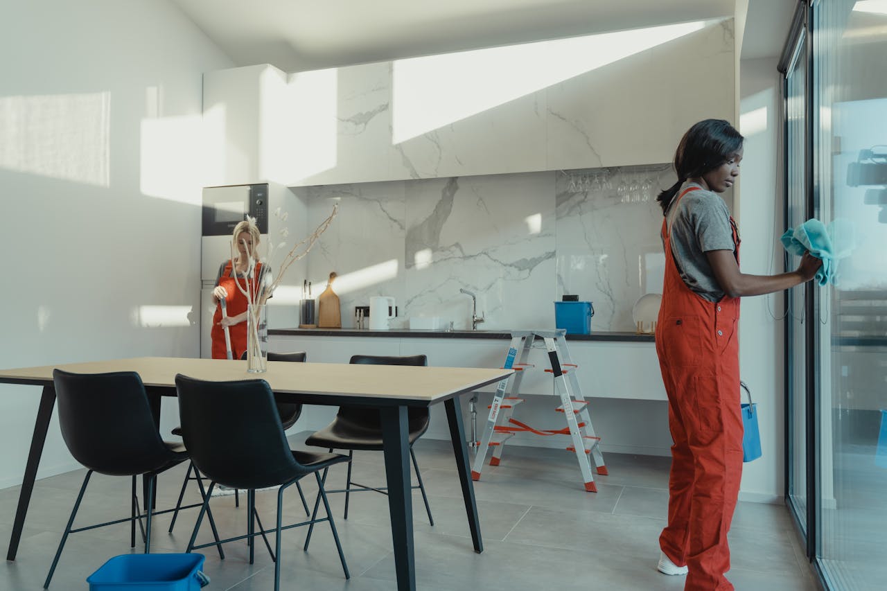 hero-img Two women in work clothes cleaning a kitchen with glass doors.